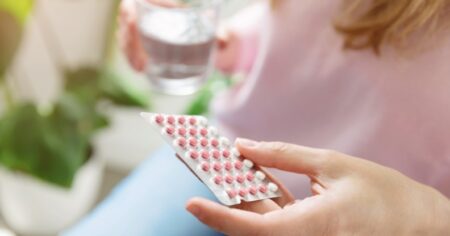 Personne se présentant comme une femme tenant une plaquette de pilules contraceptives et un verre d'eau.