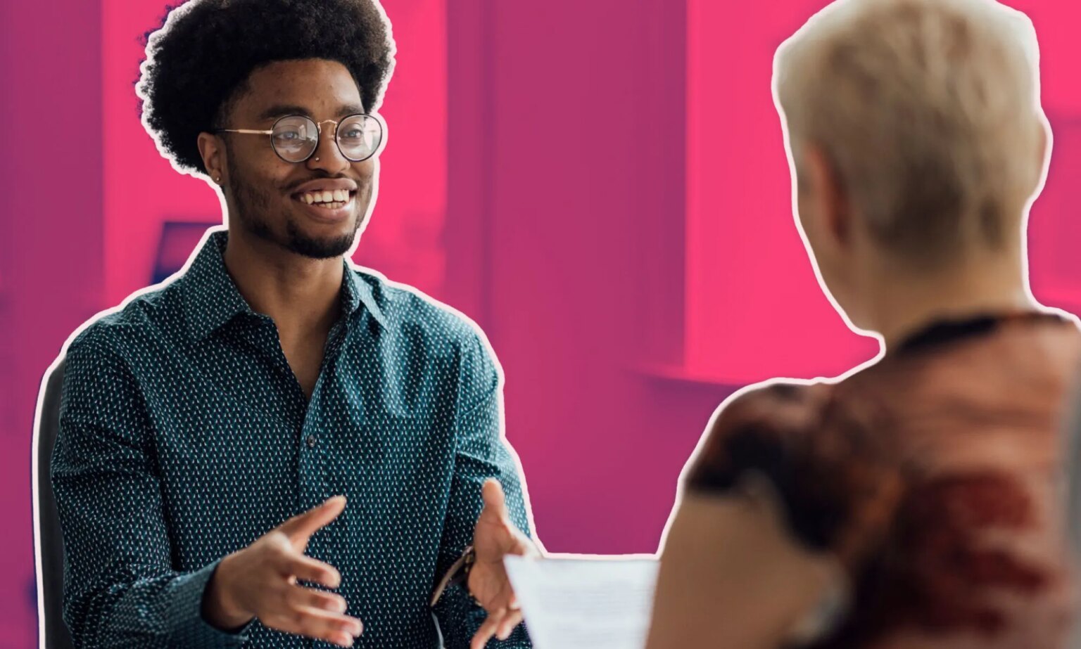 PinkNews et Amply Network de Jobbio lancent un forum d'emploi pour aider les personnes queer à trouver des employeurs inclusifs This is an image of a job interview. There is a Black man with glasses speaking to a white women with blond hair.