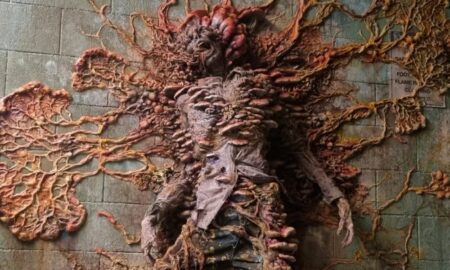 This image from The Last of Us depicts a chilling scene of a human infected by the "Cordyceps" fungus. The fungal growth has overtaken the host, transforming them into a grotesque and surreal figure. The body appears to be fused to a wall, with vibrant fungal tendrils and spores spreading outward, showcasing the invasive nature of the infection. This representation highlights the post-apocalyptic horror and the terrifying consequences of a parasitic fungus controlling its host in the game
