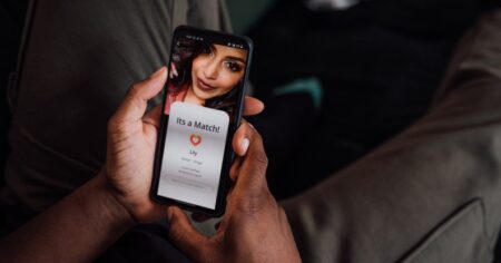 Gros plan des mains tenant un smartphone. L'écran montre qu'ils ont jumelé avec une jeune femme-présentatrice.