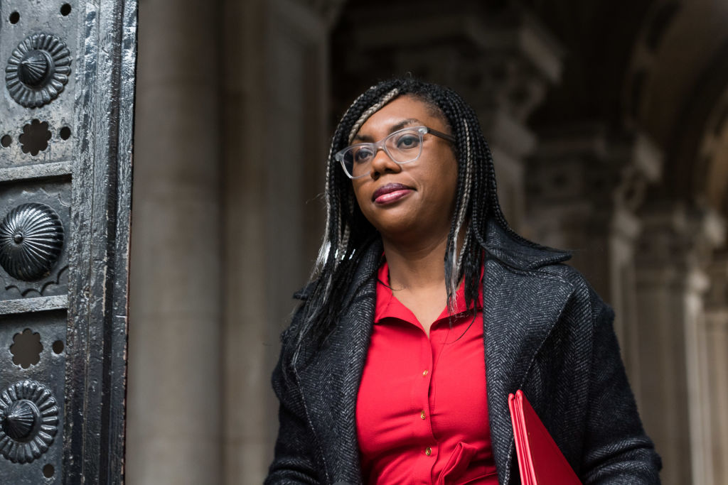 Kemi Badenoch portant un blazer noir et un chemisier rouge marchant dehors.