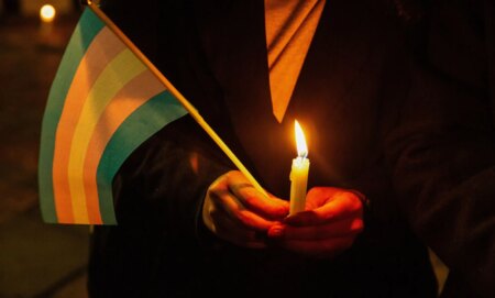 A person holding a candle and a trans flag.