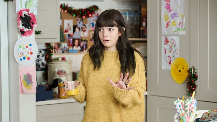 Ramona Marquez dans le rôle de Karen dans un pull jaune dans la cuisine