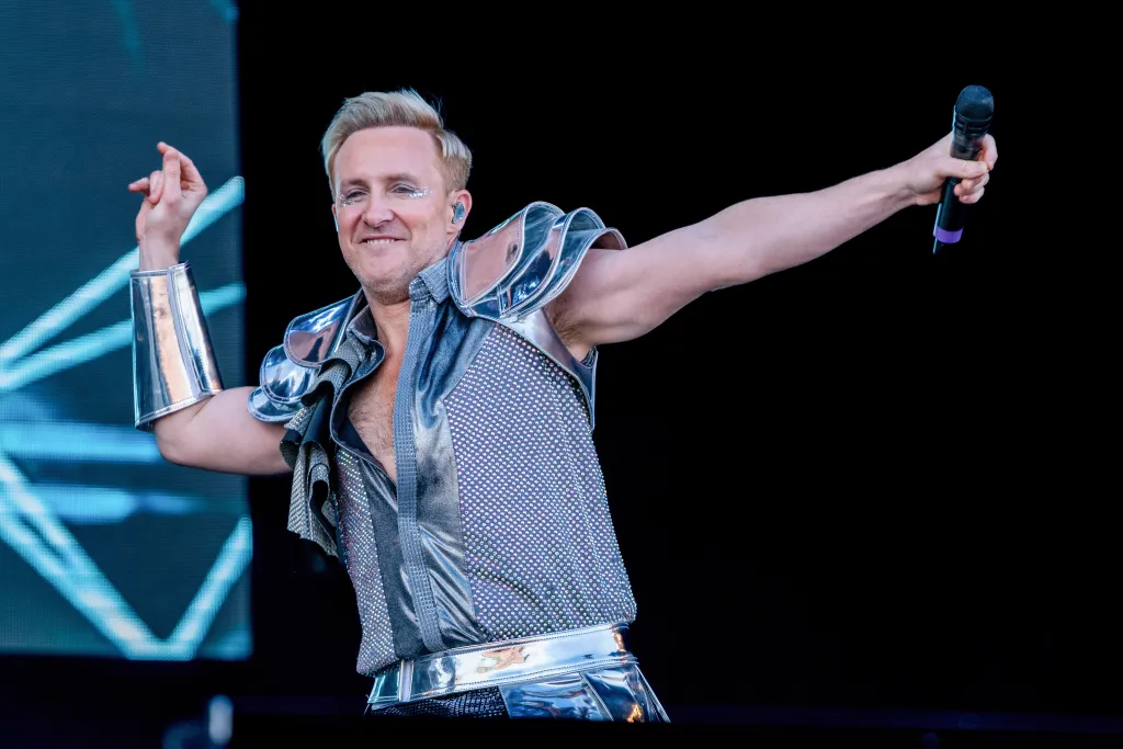 H du groupe Steps se produit sur la scène principale du Car Fest South. Il porte une tenue argentée avec des brassards et des épaulettes d'aspect métallique.