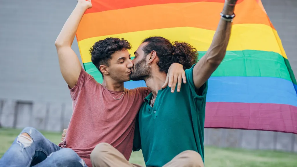 Image de deux hommes s'embrassant sous un drapeau de la fierté