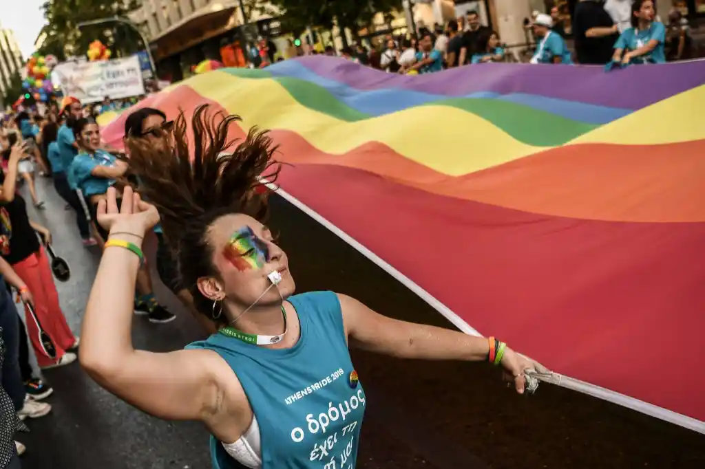 Un participant danse en tenant un grand drapeau arc-en-ciel lors de la Gay Pride d'Athènes