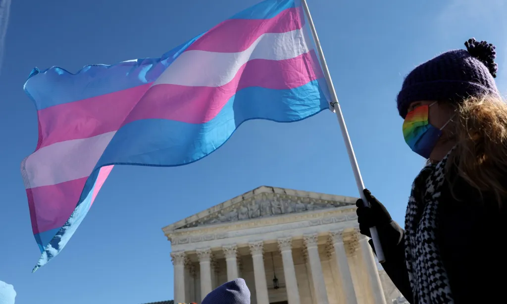 Une personne devant la Cour suprême agitant un drapeau trans.