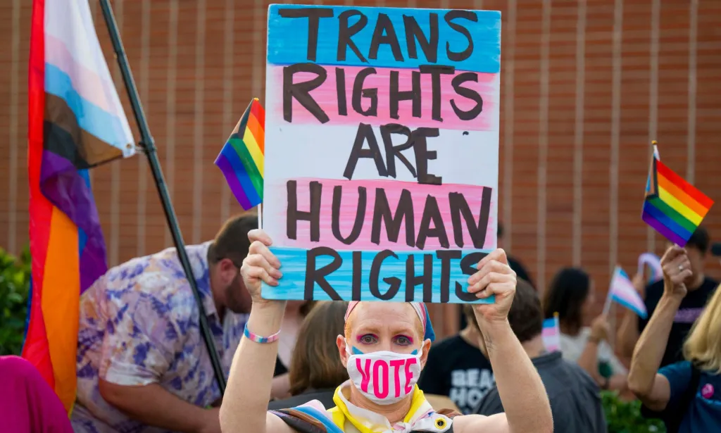 Une personne brandit une pancarte indiquant « Les droits des trans sont des droits de l’homme » lors d’une manifestation en Californie