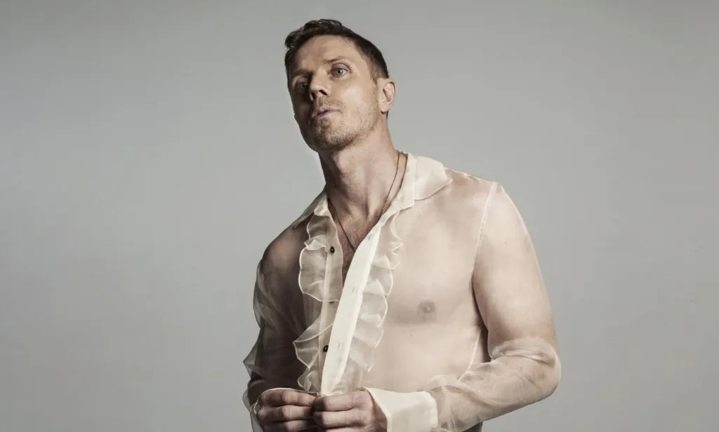 Jake Shears porte un haut blanc transparent à volants dans une image promotionnelle pour son nouvel album Last Man Dancing.