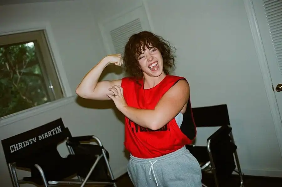 Sydney Sweeney sur le tournage du biopic sans titre sur Christy Martin ; portant un pantalon de survêtement gris et un gilet rouge, fléchissant ses biceps.