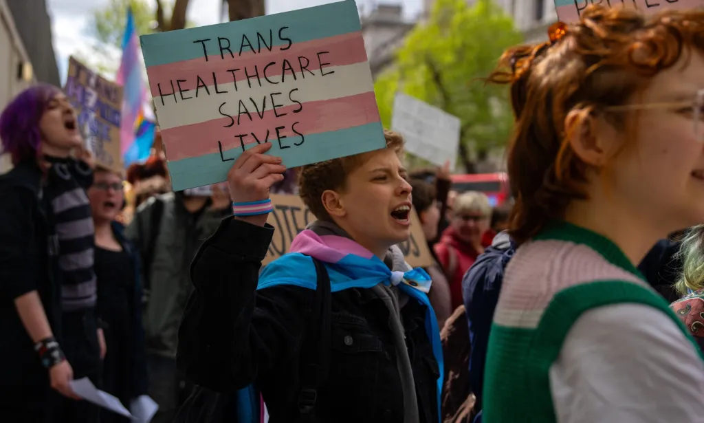 Des manifestants brandissent des pancartes sur lesquelles on peut lire « Les soins de santé trans sauvent des vies ».