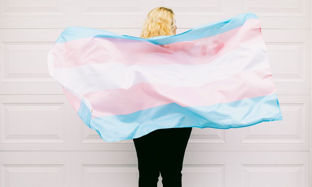 Une personne portant un drapeau trans comme cape.