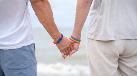 Back view gay couple holding hands at the beach.