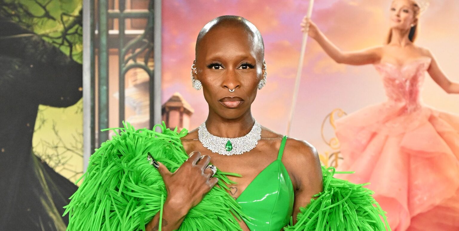Cynthia Erivo on a red carpet at a Wicked premiere in a green dress and matching feather boa staring at the camera