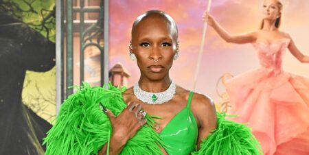 Cynthia Erivo on a red carpet at a Wicked premiere in a green dress and matching feather boa staring at the camera