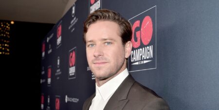 Armie Hammer on a red carpet in 2019 looking at the camera side ways on.