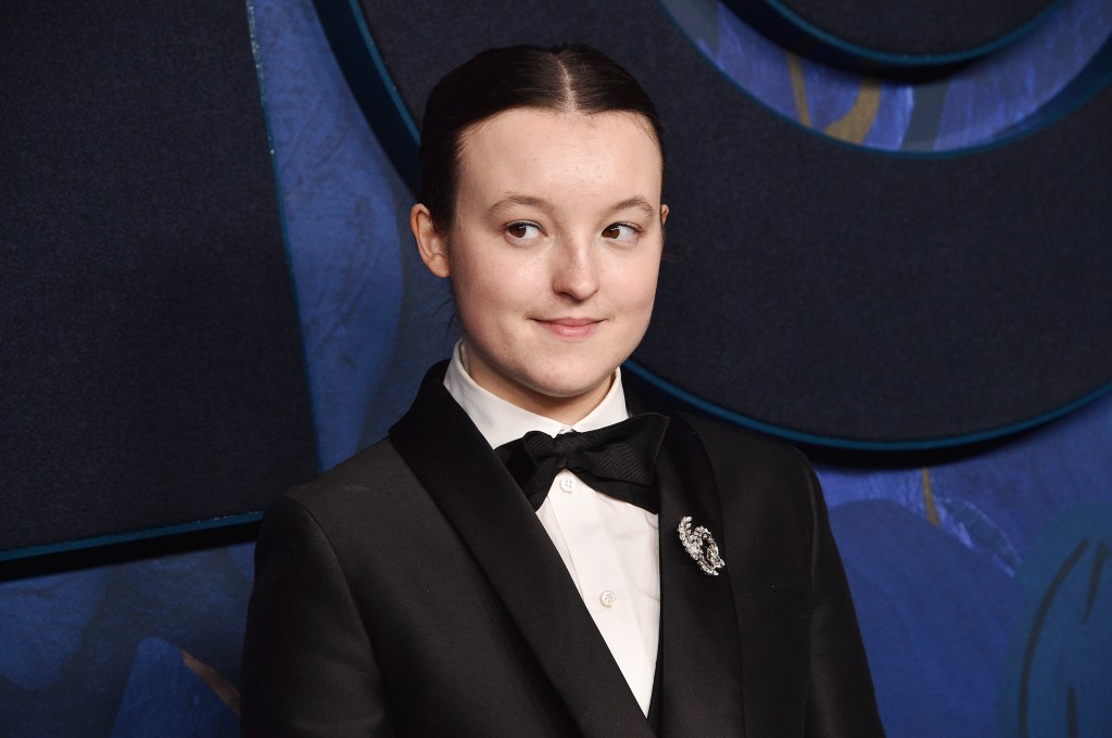 Bella Ramsey dans une chemise blanche et un costume noir et un nœud papillon. Leurs cheveux sont attachés et ils regardent à leur droite.