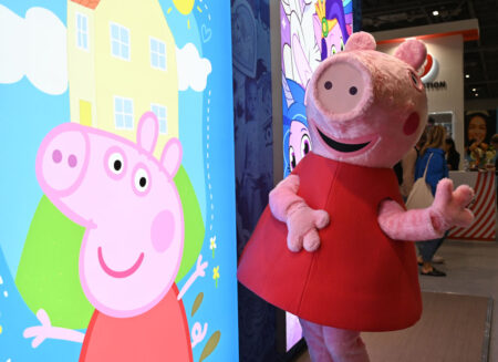 A person dressed as Peppa Pig stands by an illuminated sign