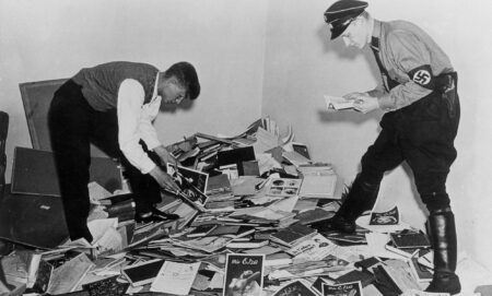 Nazi demonstrators stand above a pile of books, papers and research about the trans community during WWII