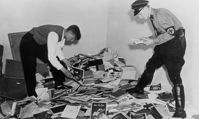 Nazi demonstrators stand above a pile of books, papers and research about the trans community during WWII