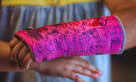 A young person with a pink cast for a broken wrist that has been drawn on.