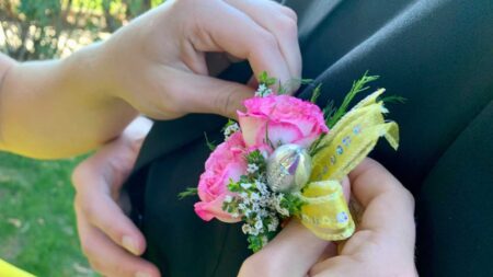 Teenage female, age 17-18, pinning floral boutonnière on Homecoming date suit lapel.