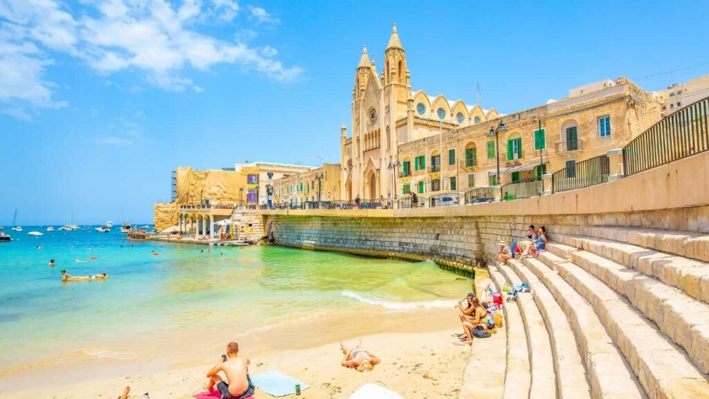 Balluta Bay beach in St Julian's town, Malta travel photo with young people chilling on the beach.