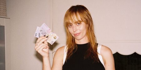 Gordi in a black vest top holding up notes of cash and smiling.