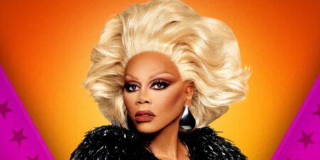 RuPaul in a black frilly coat and coiffed blonde hair in the promotional photo for Drag Race All Stars 10. She is posing against an orange and pink background.