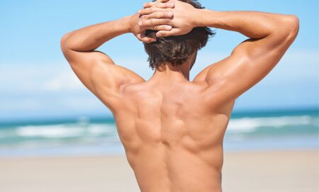 A naked man flexing on a beach.