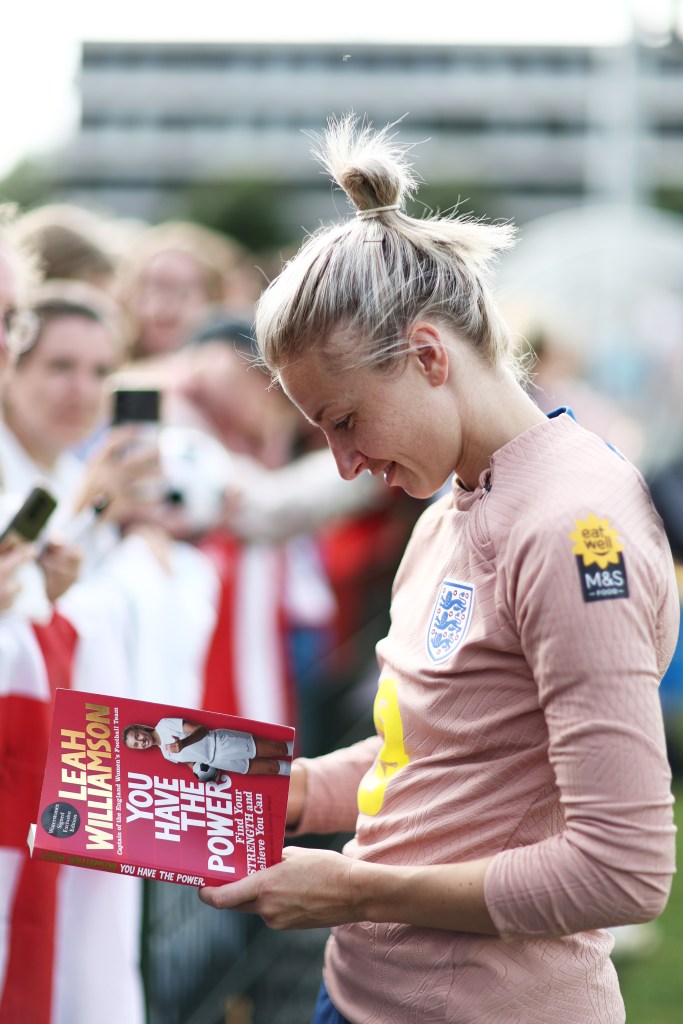 Leah Williamson d'Angleterre examine une copie de son livre alors qu'elle salue les fans après une session d'entraînement