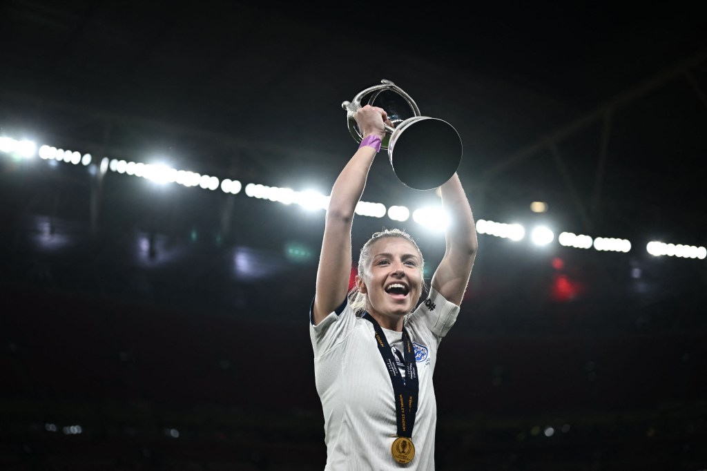 Leah Williamson célèbre avec le trophée après la victoire de l'Angleterre dans le "Finalissima". Elle porte un haut blanc, une médaille autour de son cou et soulevant un trophée.