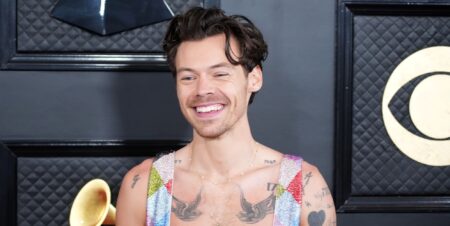 Harry Styles in a rainbow jumpsuit smiling.