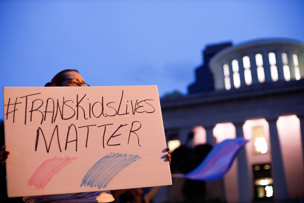 Le militant des droits trans détenant un signe qui se lit comme suit "Trans Kids Lives Matter".