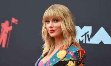 Taylor Swift on the red carpet wearing a patterned pastel blazer and bright red lip stick in 2019.