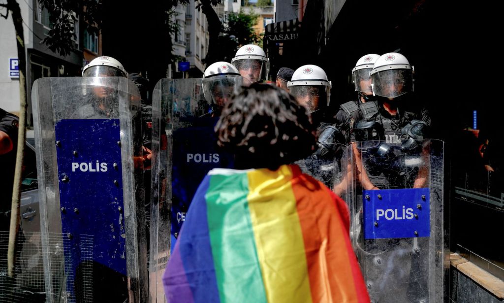 Une personne LGBTQ + avec un drapeau de fierté sur leurs épaules se levant à la police tenant des boucliers anti-émeute en Turquie.