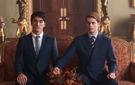 Red, White & Royal Blue still: Alex (Perez) and Prince Henry (Galitzine) sat on a royal red and gold sofa, both wearing suits. Henry has stretched his arm to hold Alex