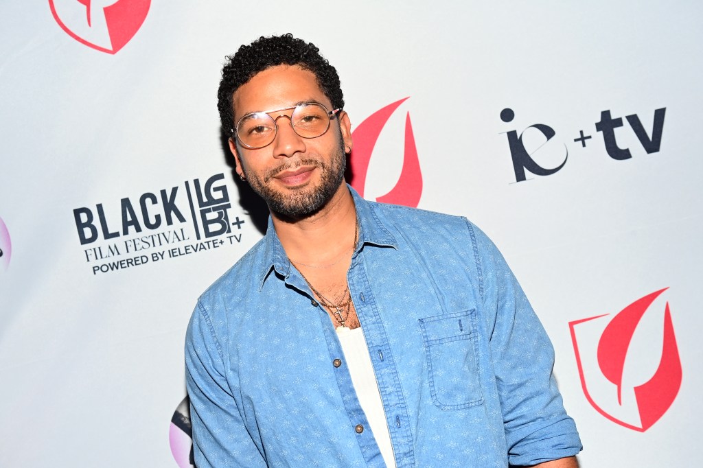 Jussie Smollett portant une veste en jean sur un gilet blanc. Il porte également des lunettes en argent teintées.