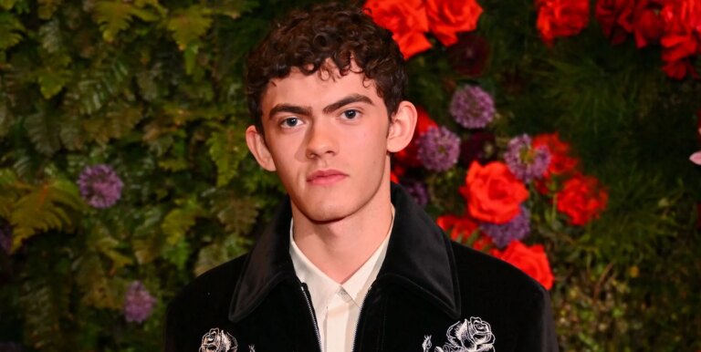 Joe Locke poses in a black jacket and white shirt against a flowery background.