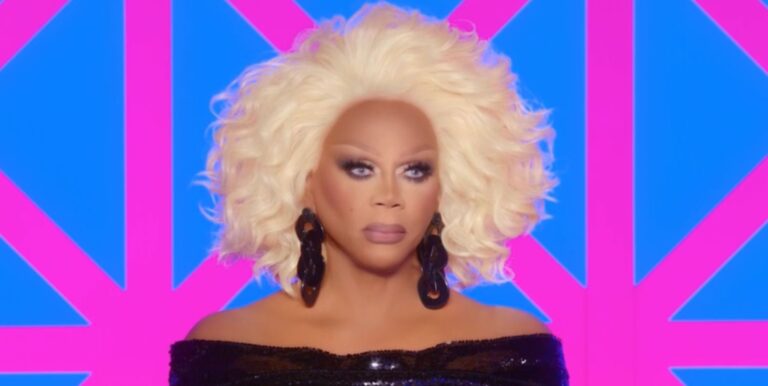 RuPaul on the Drag Race UK judging panel looking solemn, wearing a glittering black ress and earrings.