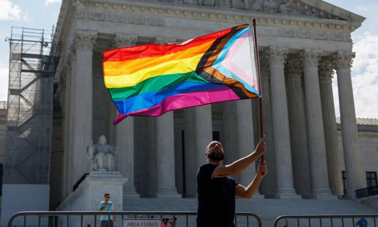 La Cour suprême fixe une date pour examiner la contestation du mariage homosexuel : ce que cela signifie et ce qui se passera ensuite Someone holding an LGBTQ+ flag outside the Supreme Court.