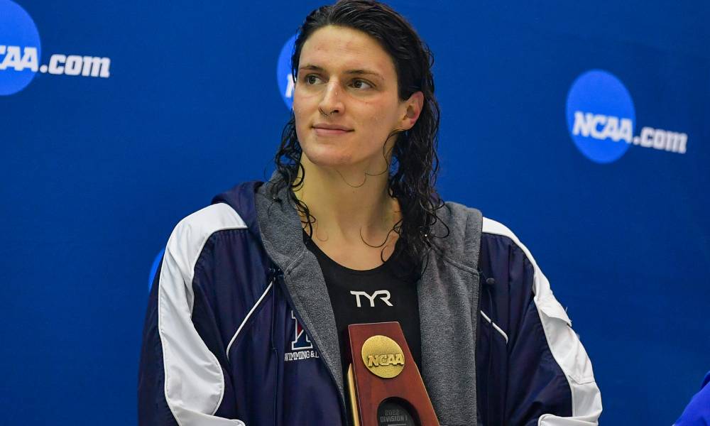 Lia Thomas, nageuse de l'Université de Pennsylvanie, tient un trophée de la NCAA tout en regardant sur le côté