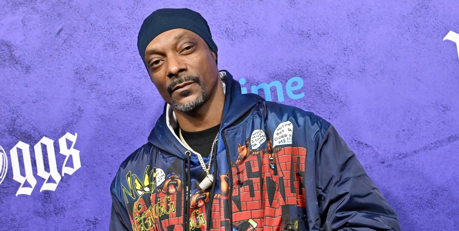 NBC met fin à l'émission spéciale du Nouvel An de Snoop Dogg Snoop Dog in a blue yello and red denim jacket at a premiere with a purple background behind him.