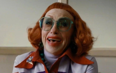 Weapons still of Aunt Gladys with bright red hair and micro-bangs, smudged red lipstick and bright teal glasses.