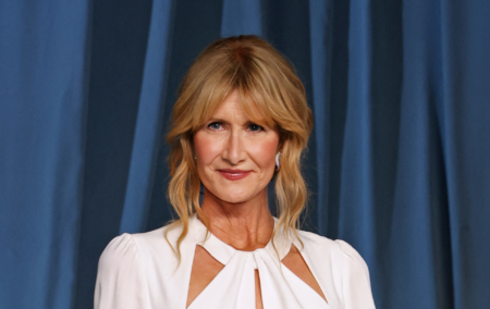 Laura Dern against a blue curtain background wearing a white dress.