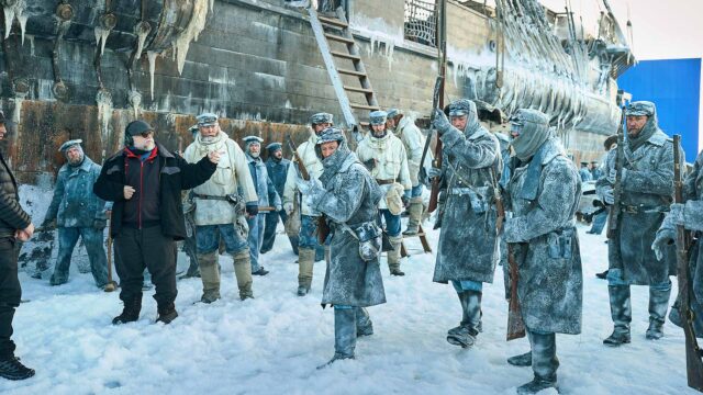 FRANKENSTEIN. (De gauche à droite) le scénariste/réalisateur Guillermo del Toro Lars Mikkelsen en tant que capitaine Anderson, Nikolaj Lie Kaas en tant que chef de la direction avec des acteurs sur le tournage de Frankenstein. Cr. Ken Woroner/Netflix © 2025.