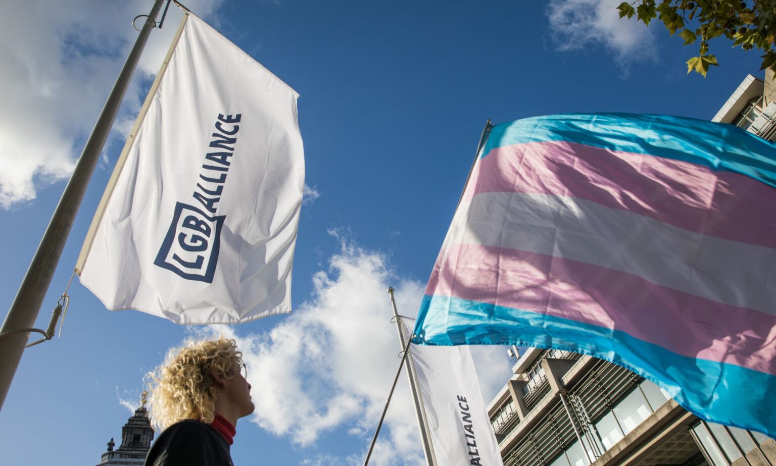 LGB Alliance affirme que l’interdiction des toilettes trans n’affectera pas les personnes cis – mais c’est déjà le cas An LGB Alliance waves next to a trans flag.