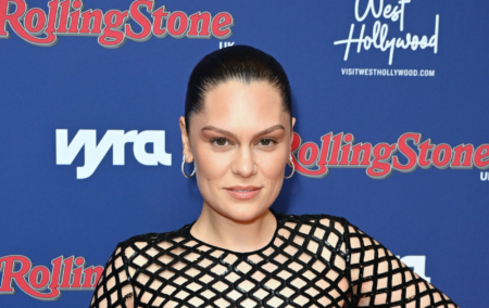Jessie J posing on red carpet, hair pulled back, wearing silver hoop earrings and black sequin fishnet top.