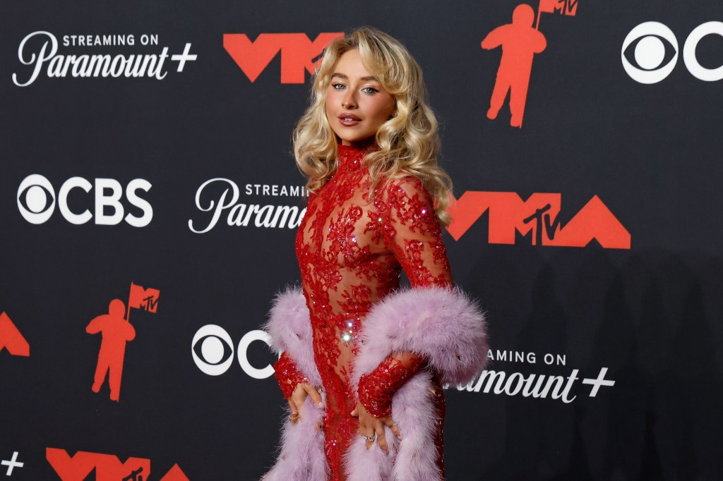 Sabrina Carpenter dans une robe rouge brodée de bijoux et une écharpe violette moelleuse sur les bras.