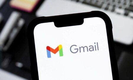 Someone holding a phone in front of a laptop with the Gmail logo visible.